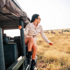 A woman sitting on top of a jeep in the wild